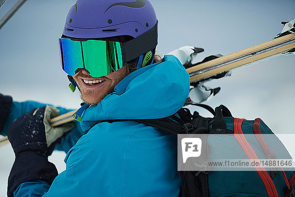 Männlicher Skifahrer mit Skiern  über die Schulter blickend  Porträt  Alpe-d'Huez  Rhône-Alpes  Frankreich