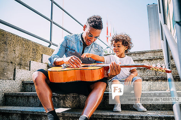 Father teaching son play guitar on stairway
