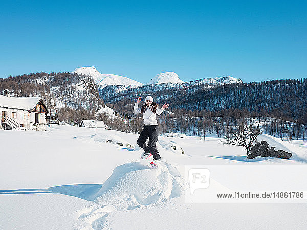 Junge Frau mit Strickmütze springt in schneebedeckter Landschaft  Porträt  Alpe Ciamporino  Piemont  Italien