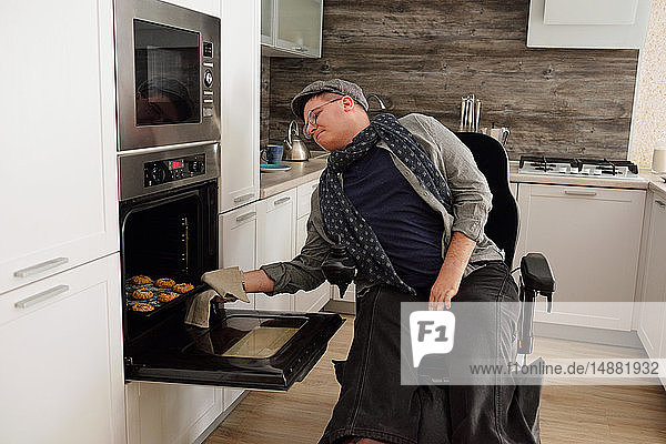 Körperlich behinderter Mann entfernt Tablett mit Keksen aus dem Ofen in der Küche