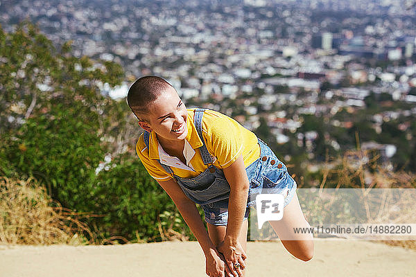 Teenage girl with cropped hair balancing on one leg on cityscape hilltop  Los Angeles  California  USA