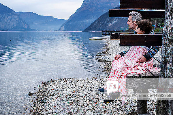 Junge und Vater eingewickelt in eine Decke am Seepier  Seitenansicht  Comer See  Onno  Lombardei  Italien