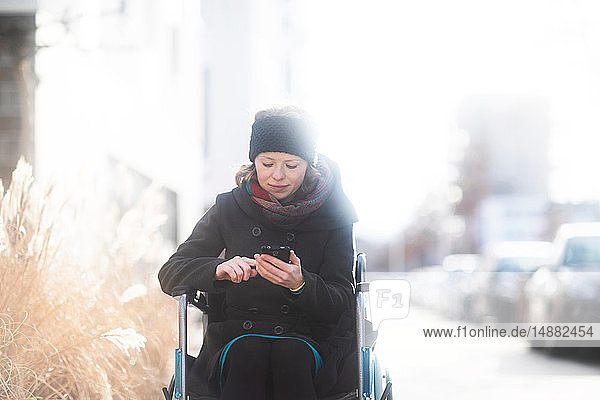 Frau im Rollstuhl mit Mobiltelefon auf der Strasse