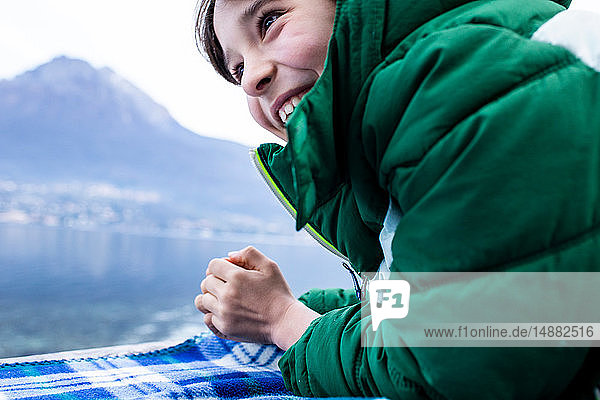 Junge in grünem Anorak auf einer Picknickdecke am Seeufer liegend  beschnitten  Comer See  Onno  Lombardei  Italien