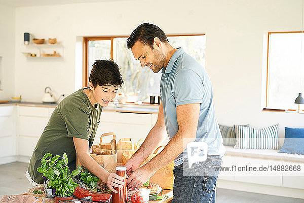 Junge und sein Vater an der Küchentheke beim Auspacken von Lebensmitteln
