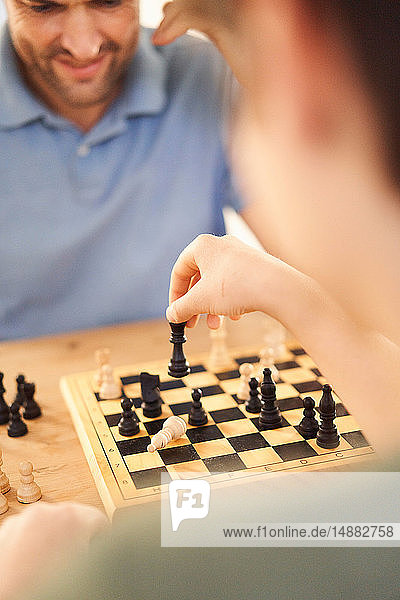 Junge und Vater spielen eine Schachpartie am Wohnzimmertisch  über der Schulter aus nächster Nähe