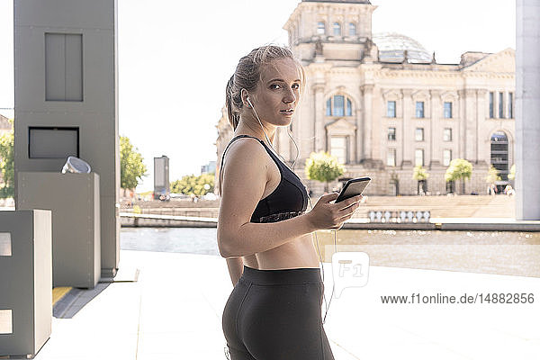 Junge Frau macht Pause vom Sport und benutzt Smartphone in der Stadt  Berlin  Deutschland