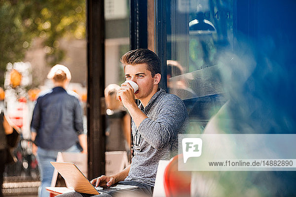 Junger Mann trinkt Kaffee und benutzt Laptop im Café