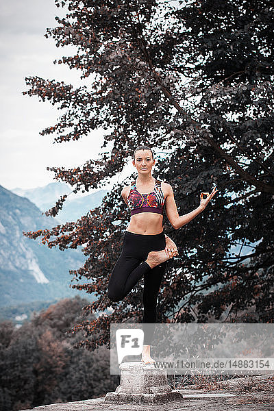 Frau praktiziert Yoga  balanciert auf einem Bein auf einem Sockel  Berglandschaft  Domodossola  Piemont  Italien