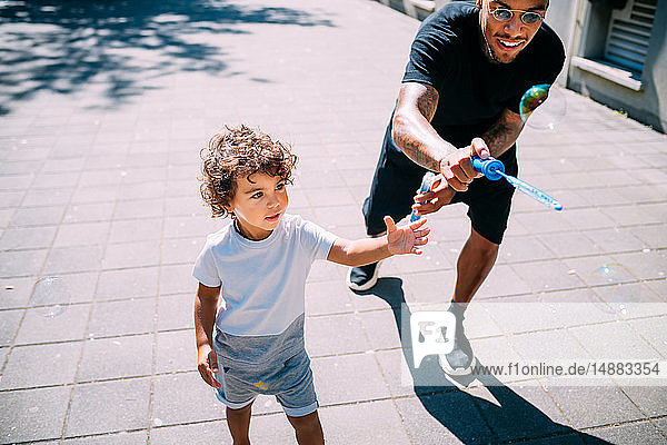 Father and son playing with soap bubbles on sidewalk