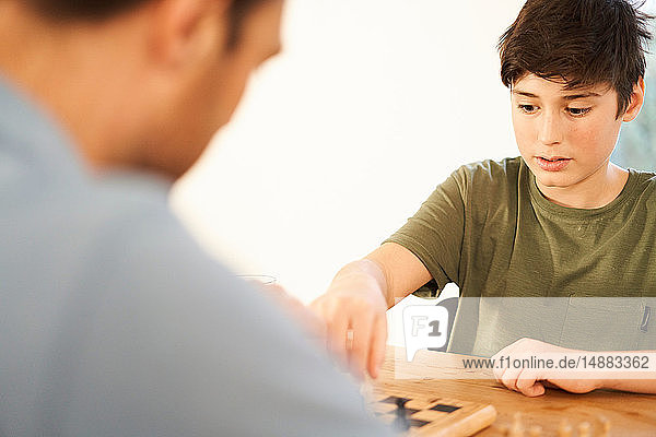 Boy and father playing chess at living room table over shoulder view