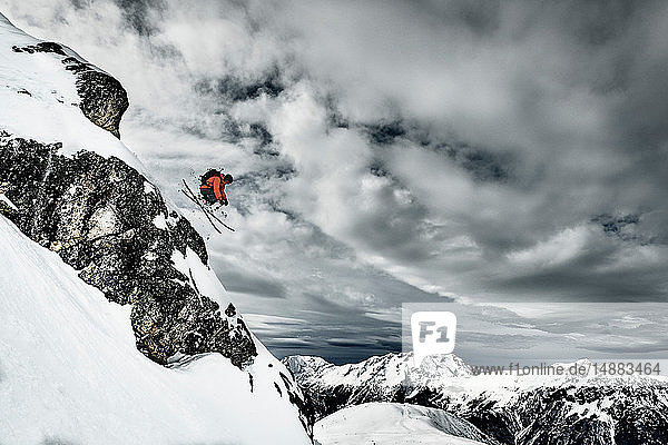 Männlicher Skifahrer springt in der Luft von einem schroffen Berghang  Alpe-d'Huez  Rhône-Alpes  Frankreich