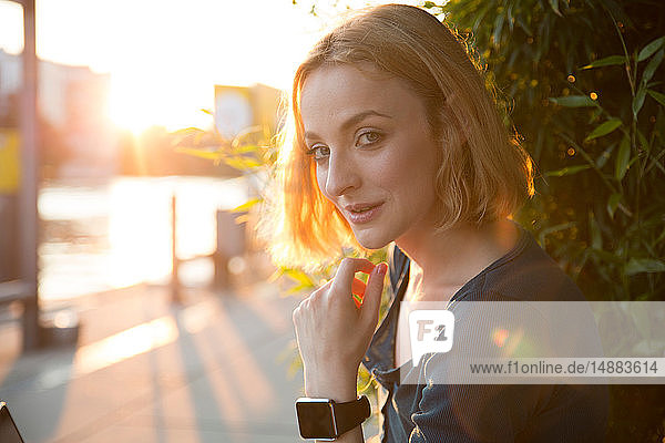 Junge Frau mit Smartwatch sitzt vor einem Café
