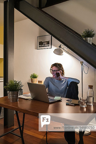 Woman working at laptop and talking on cellphone in home office