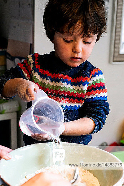 Kleinkind gießt Wasser in Mehl in Rührschüssel