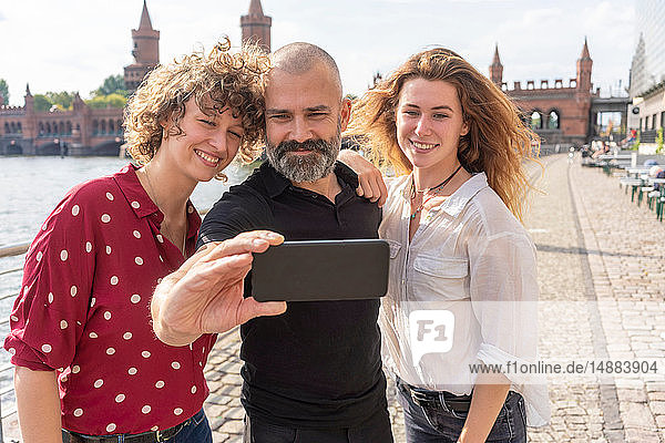 Man and female friends taking selfie with smartphone on bridge  river and buildings in background  Berlin  Germany