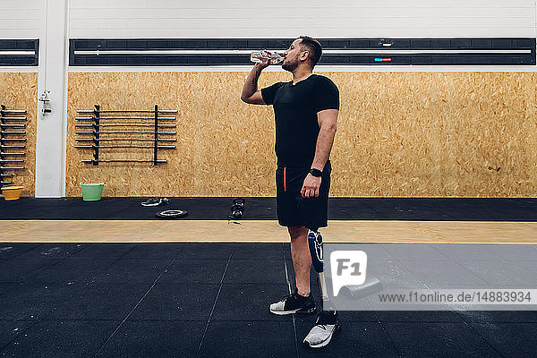 Mann mit Beinprothese trinkt Wasser im Fitnessstudio