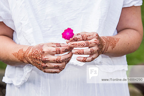 Frau in weißem Kleid mit Henna-Tattoo auf Händen  die eine Blume halten