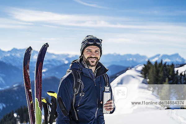 Deutschland  Bayern  Brauneck  Porträt eines lächelnden Mannes auf einer Skitour im Winter in den Bergen bei einer Pause