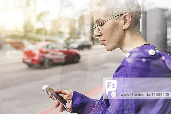 Junge Frau  die an der Bushaltestelle in der Stadt auf ihr Telefon schaut