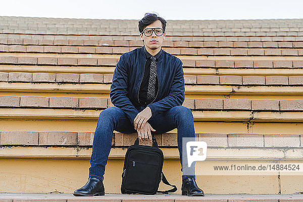 Porträt eines modischen jungen Geschäftsmannes mit Rucksack auf einer Treppe sitzend