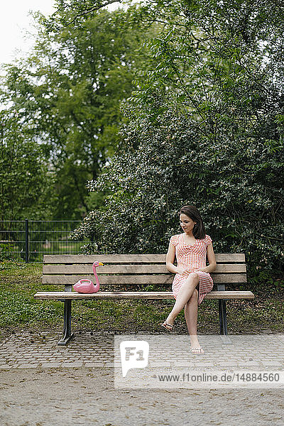 Frau sitzt auf Parkbank und unterhält sich mit rosa Flamingo-Figur