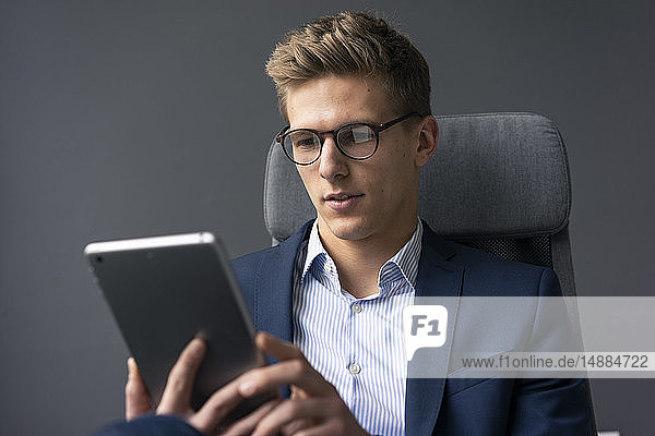 Junger Geschäftsmann sitzt auf Bürostuhl mit Tablett