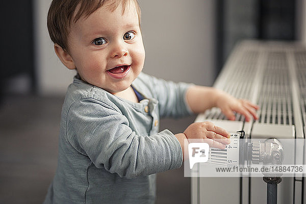 Porträt eines lächelnden kleinen Jungen  der mit dem Thermostat einer Heizung spielt