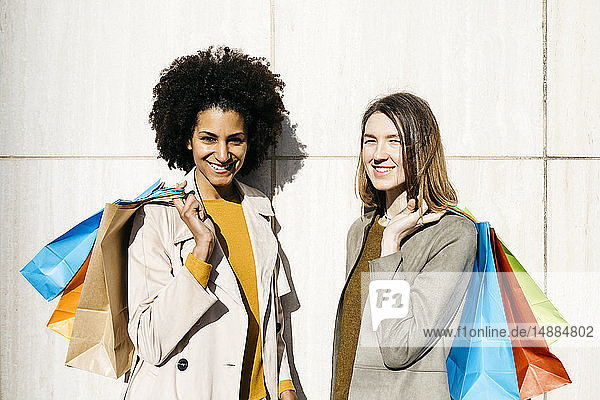 Portrait of two happy women with shopping bags standing at a wall