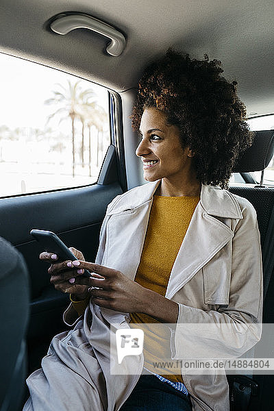 Smiling woman sitting in back seat of a car holding cell phone