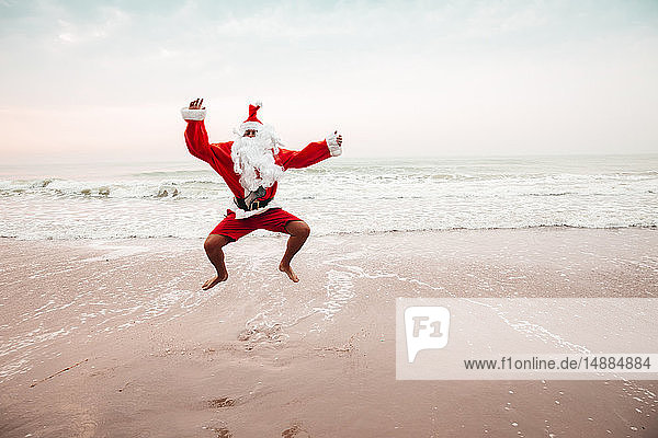 Thailand  als Weihnachtsmann verkleideter Mann springt am Strand in die Luft