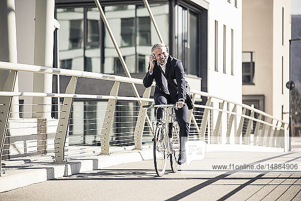 Smiling mature businessman with headphones riding bicycle on a bridge in the city