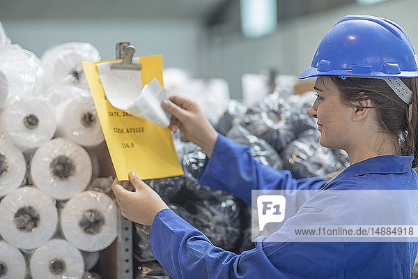 Frau mit Schutzhelm trägt Kontrolldokument in Fabrik