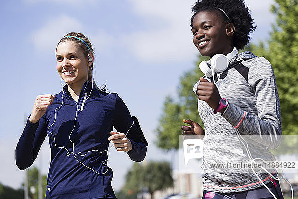 Zwei glückliche sportliche junge Frauen laufen zusammen in der Stadt