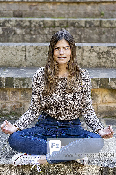 Junge Frau sitzt draußen auf einer Treppe und macht Yoga