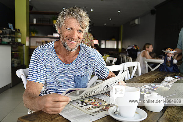 Portrait of smiling mature man sitting in a coffee shop reading newspaper