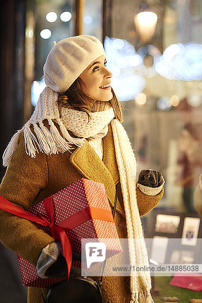 Smiling woman with Christmas present looking in shop window