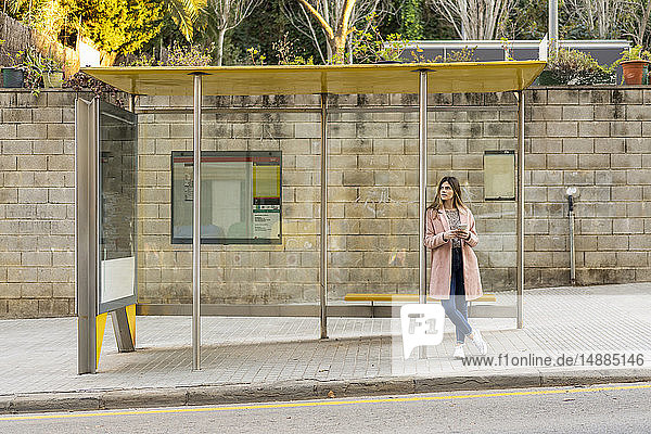 Junge Frau mit Handy wartet an Bushaltestelle