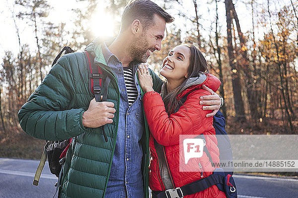 Glückliches Paar umarmt sich auf einer Straße im Wald während einer Rucksacktour