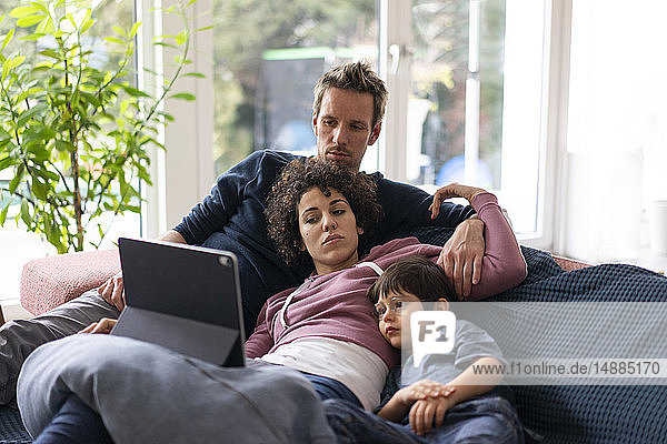 Family lying on couch watching movie on theit tablet