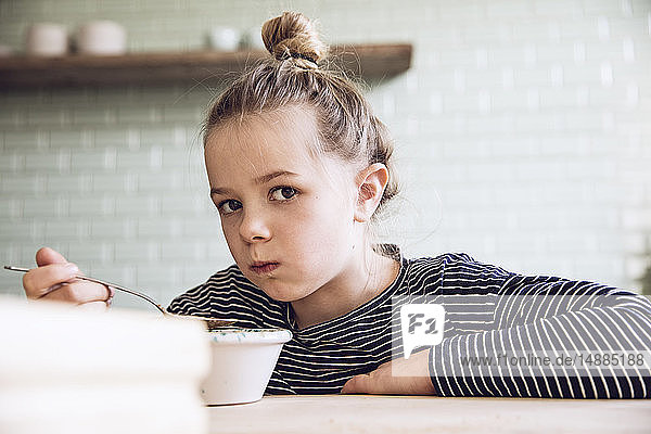 Sceptical girl sitting in kitchen  eating granola
