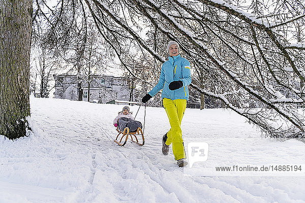 Glückliche Mutter mit Tochter auf Schlitten in Winterlandschaft