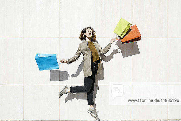 Fröhliche Frau mit Einkaufstüten  die gegen eine Wand springt