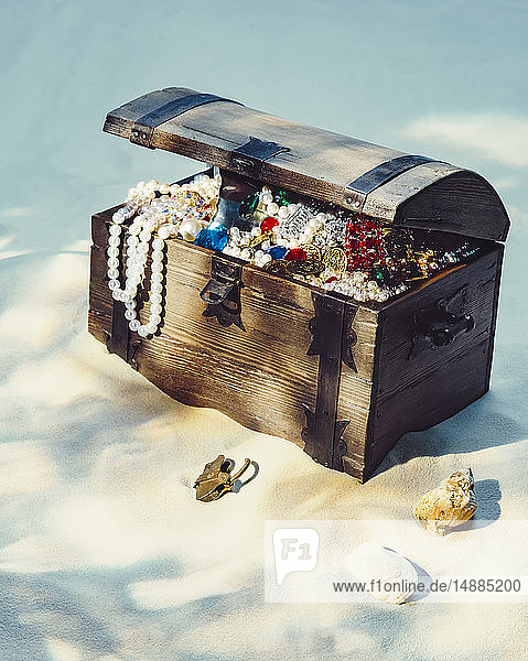 Mit Juwelen und Goldmünzen gefüllte Schatzkiste am Sandstrand