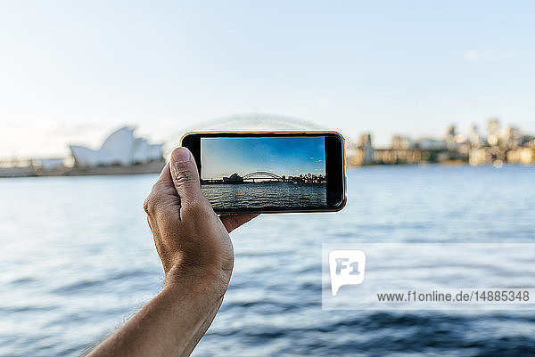 Australien  New South Wales  Sydney  Nahaufnahme eines Mannes  der ein Foto mit einem Mobiltelefon nach Sydney macht