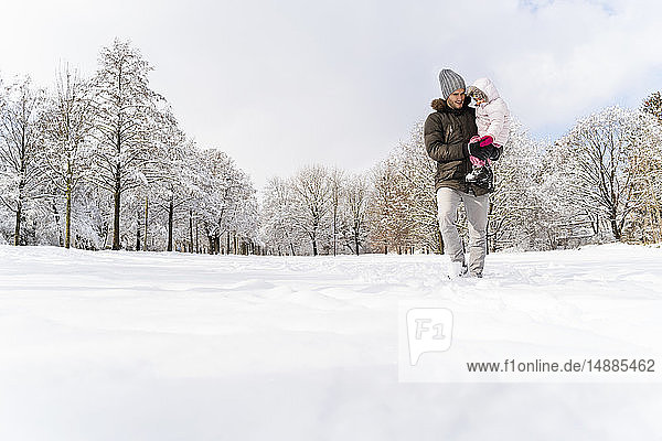 Father carrying daughter walking in winter landscape