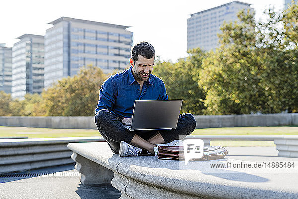 Smiling businessman sitting on bench outdoors working on laptop