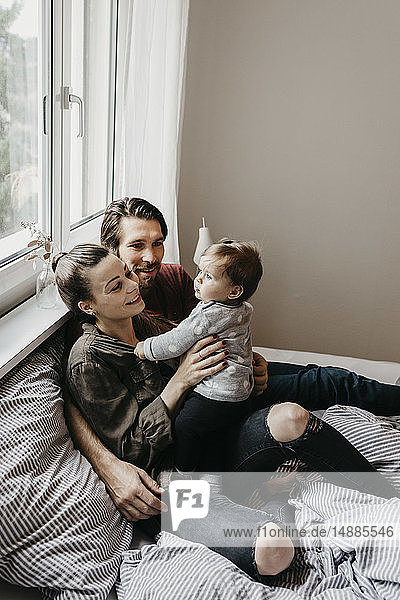 Happy family with baby girl sitting on bed at home