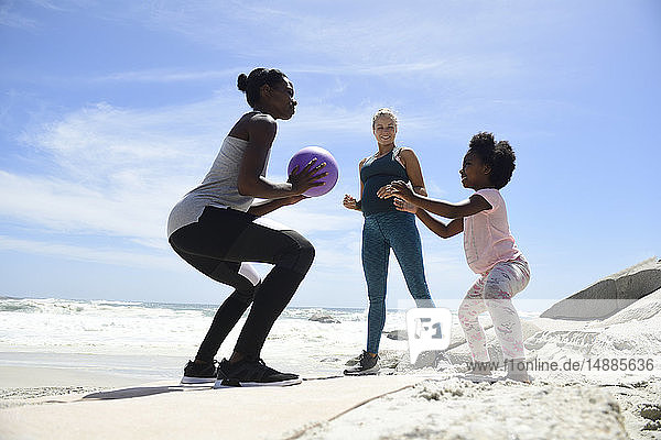 Mutter mit Tochter und Freund trainieren mit einem Ball am Strand