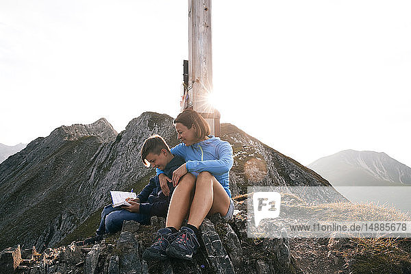 Österreich  Tirol  Mutter und Sohn auf einer Wanderung mit Buch auf dem Gipfel